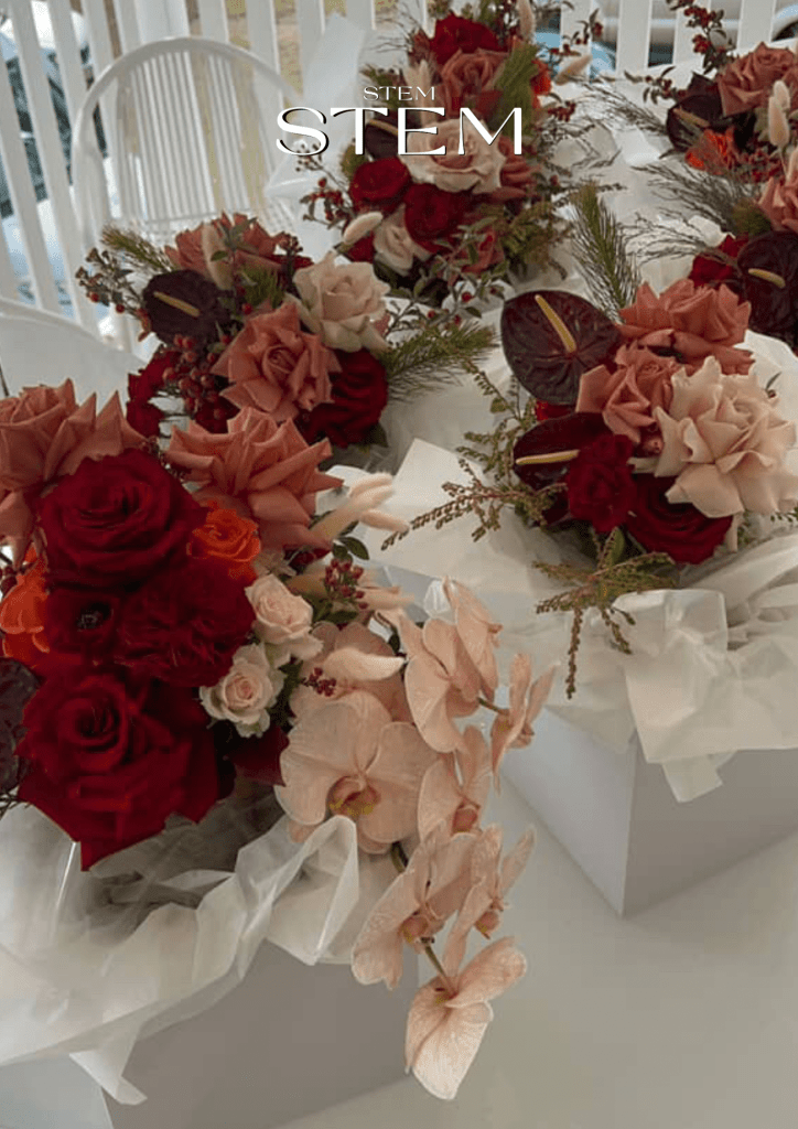 Bridal bouquets featuring deep red roses, blush pink orchids, nude roses, and burgundy anthuriums, arranged with lush greenery and textural accents.