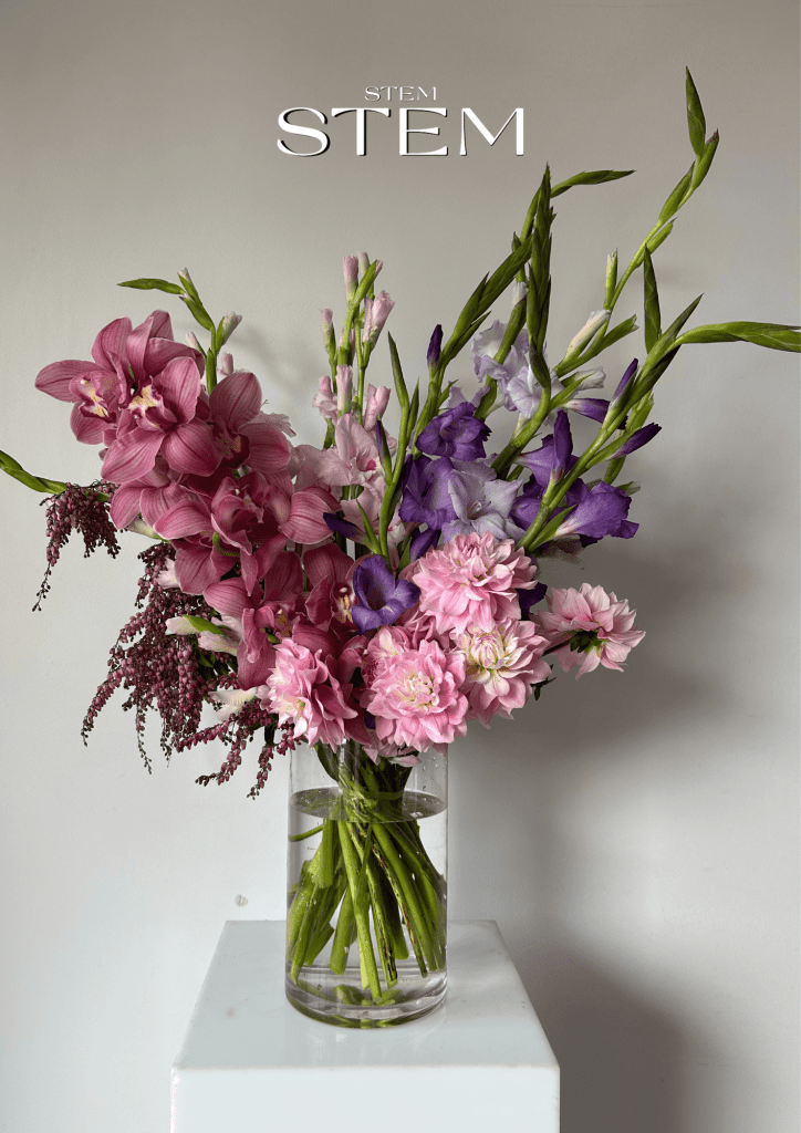 A vibrant floral arrangement of pink orchids, dahlias, and purple gladiolus in a glass vase, styled by Stem Design Brisbane.