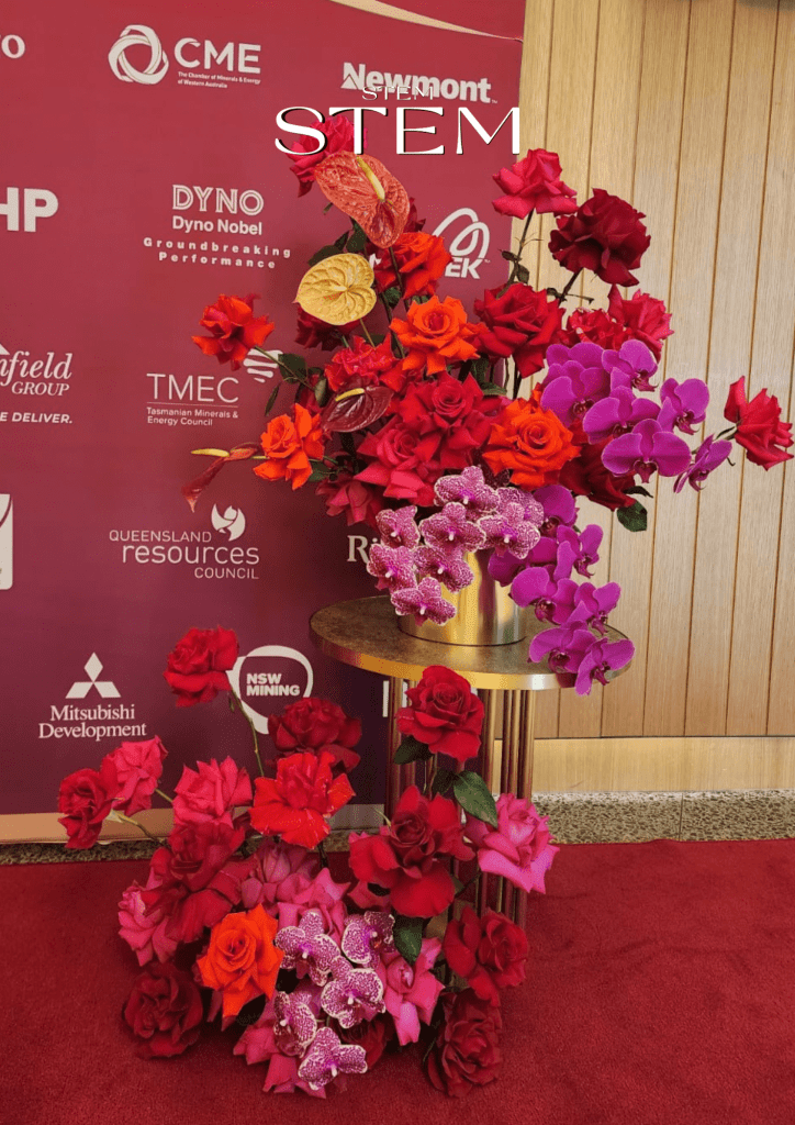 Stem Design floral installation on a media wall with red and orange roses, pink and purple orchids, vanda orchids, and anthuriums – event florist Brisbane.
