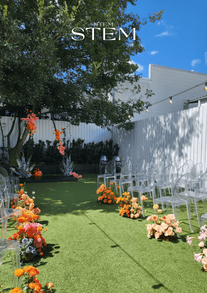 Outdoor Brisbane wedding ceremony styled with vibrant aisle flowers in orange, peach, blush, and pink, designed by Stem Design, a flexible wedding florist Brisbane with no minimum spend.