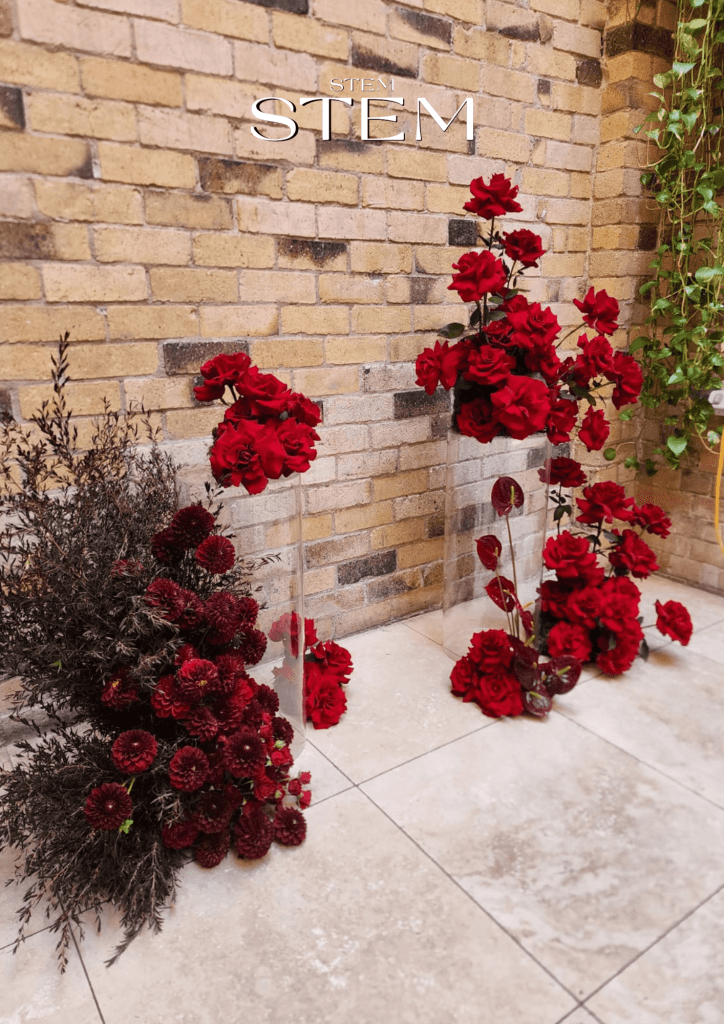 Modern red floral installation featuring roses, dahlias, and dark foliage against a brick wall, styled by Stem Design for weddings and events in Brisbane.