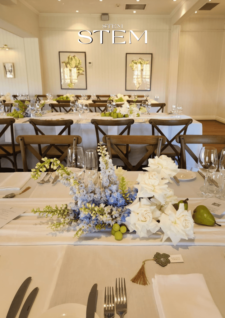 Modern wedding table styled with blue delphiniums, white roses, and pears on crisp linens, designed by Stem Design in Brisbane.