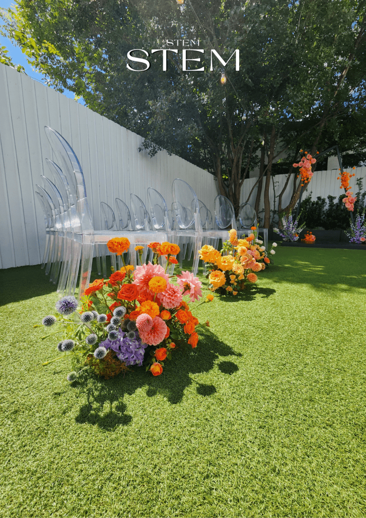 Bright and colourful wedding ceremony aisle flowers featuring dahlias, roses, billy buttons and purple globe thistles arranged on green lawn at The Joinery Brisbane.