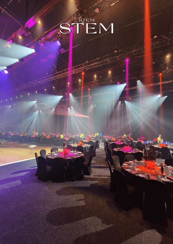 Vibrant pink and orange event flowers Brisbane styled by Stem Design featuring orchids, anthuriums, and tropical leaves under spotlight lighting.