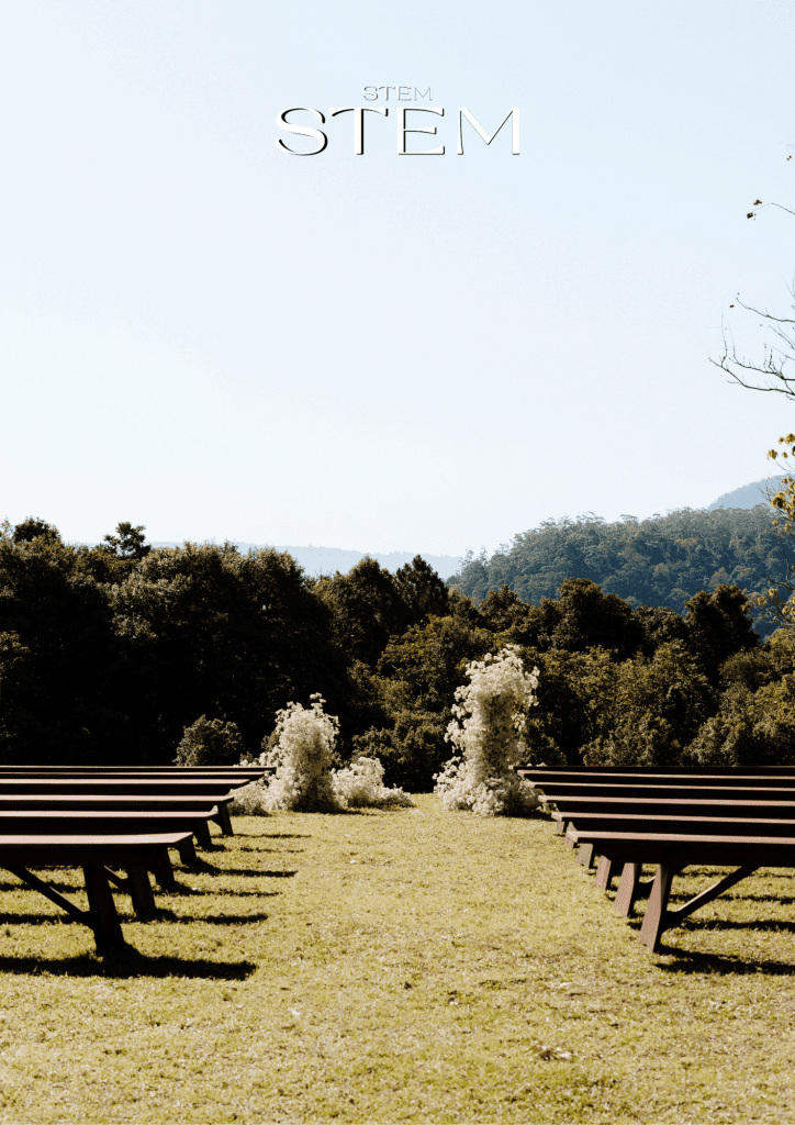 Outdoor wedding ceremony with white cloud like floral arrangements placed along the aisle against a backdrop of forest and mountain views.