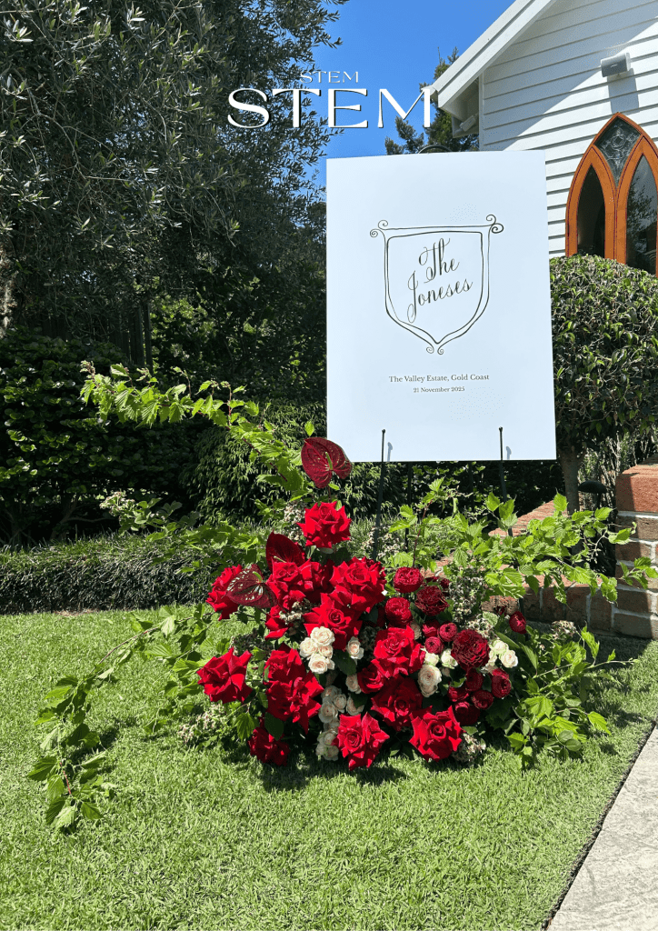 Red and burgundy wedding sign flowers displayed on the lawn at The Valley Estate on the Gold Coast, featuring roses, anthuriums and lush greenery.